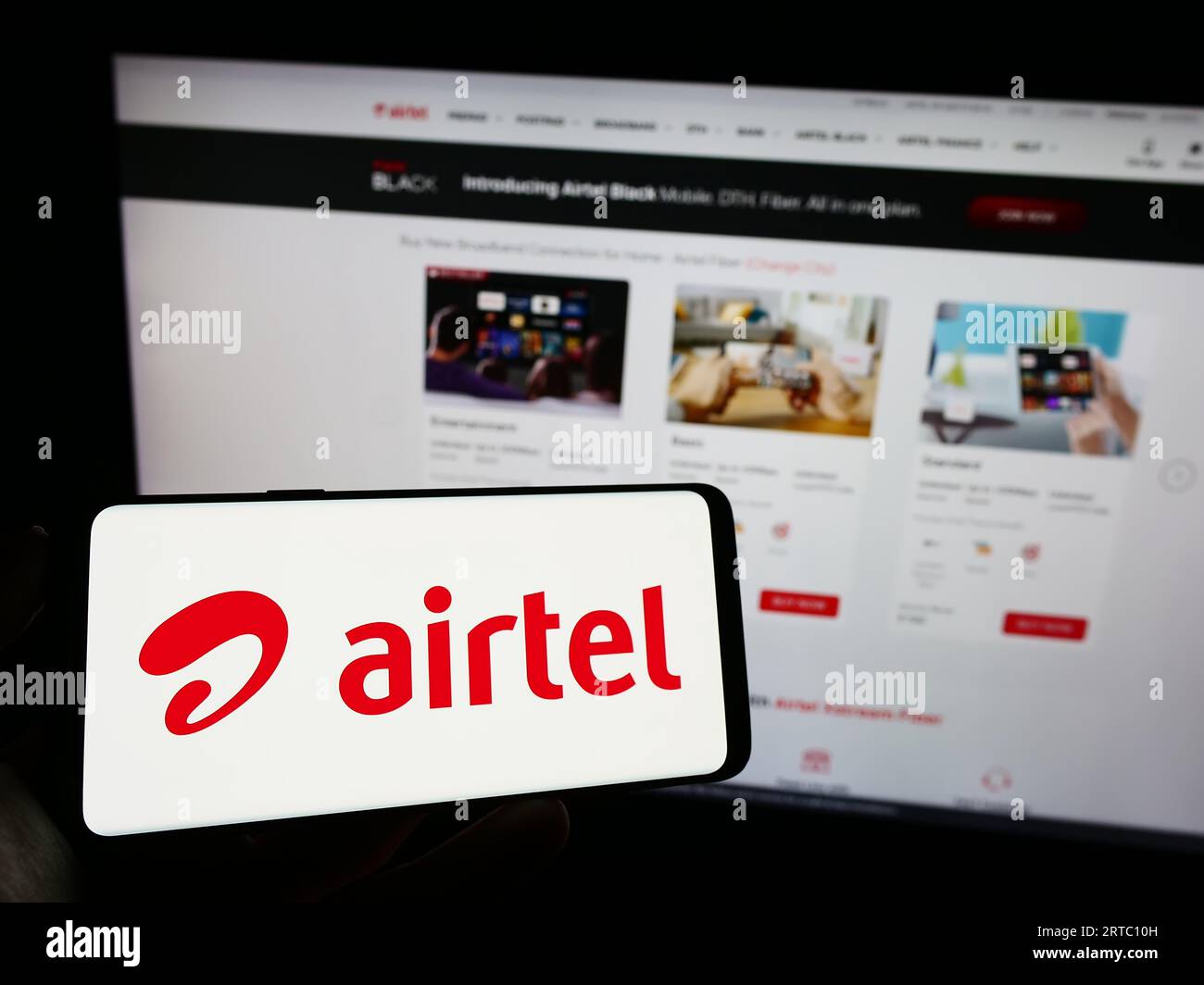 Person holding cellphone with logo of telecommunications company Bharti Airtel Limited on screen in front of webpage. Focus on phone display. Stock Photo