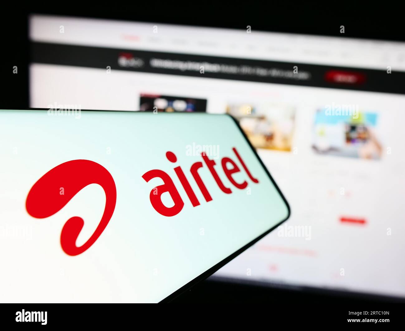 Smartphone with logo of telecommunications company Bharti Airtel Limited on screen in front of website. Focus on center-left of phone display. Stock Photo