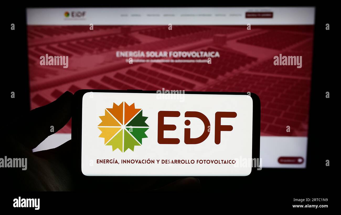 Person holding smartphone with logo of Spanish photovoltaics company EiDF Solar on screen in front of website. Focus on phone display. Stock Photo