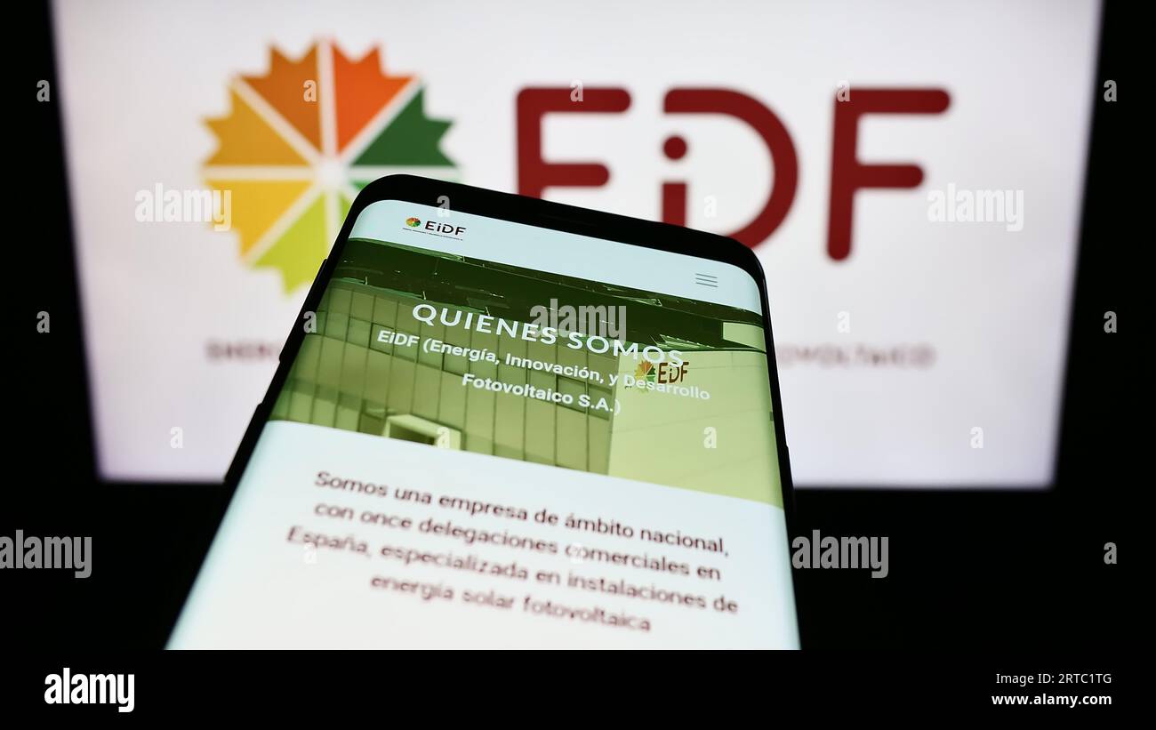 Smartphone with website of Spanish photovoltaics company EiDF Solar on screen in front of business logo. Focus on top-left of phone display. Stock Photo