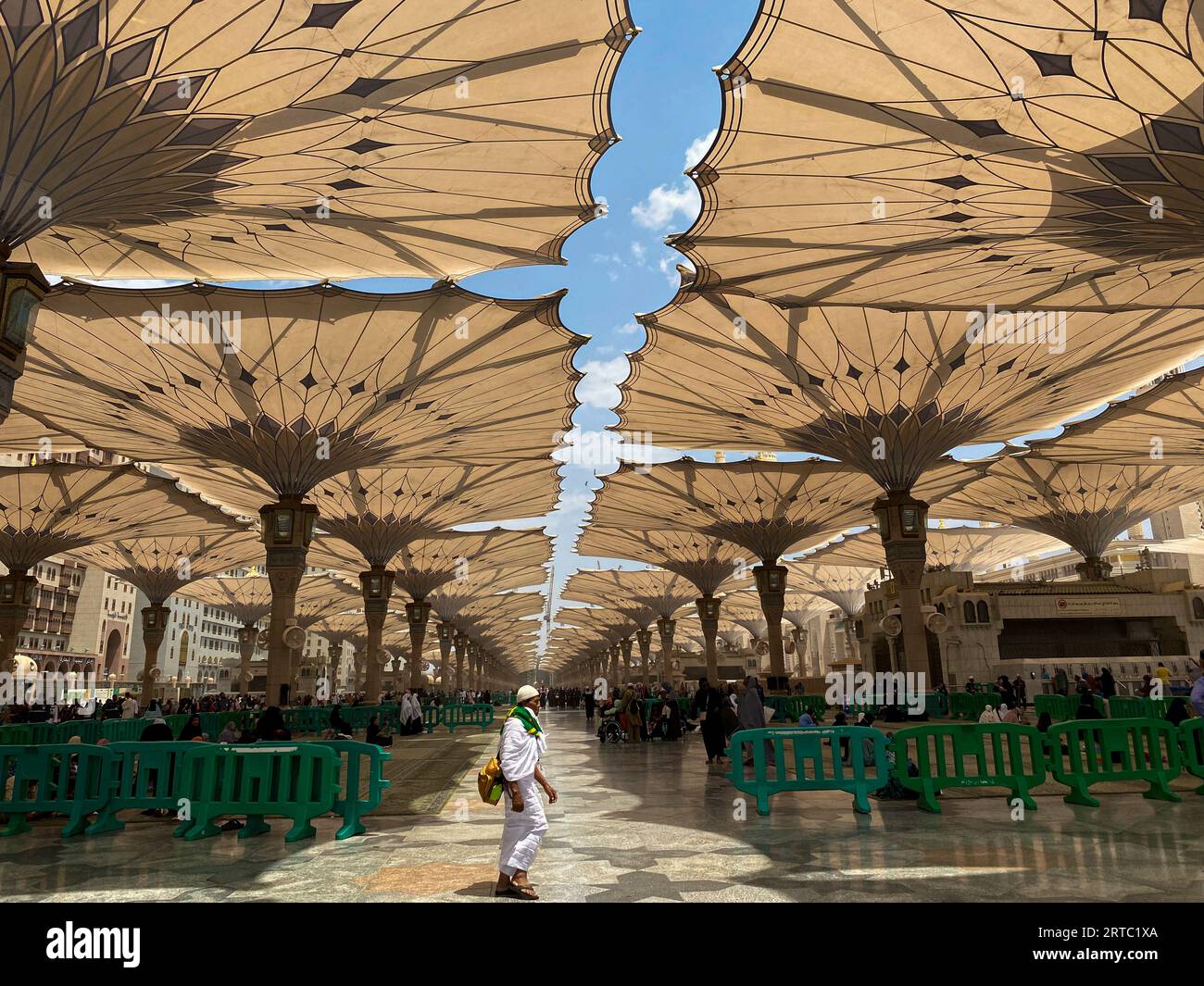 Medina, Saudi Arabia - August 22, 2023: Pilgrims walk underneath giant umbrellas at Nabawi Mosque compound. Canopies at Masjid Nabawi in Medina, Saudi Stock Photo