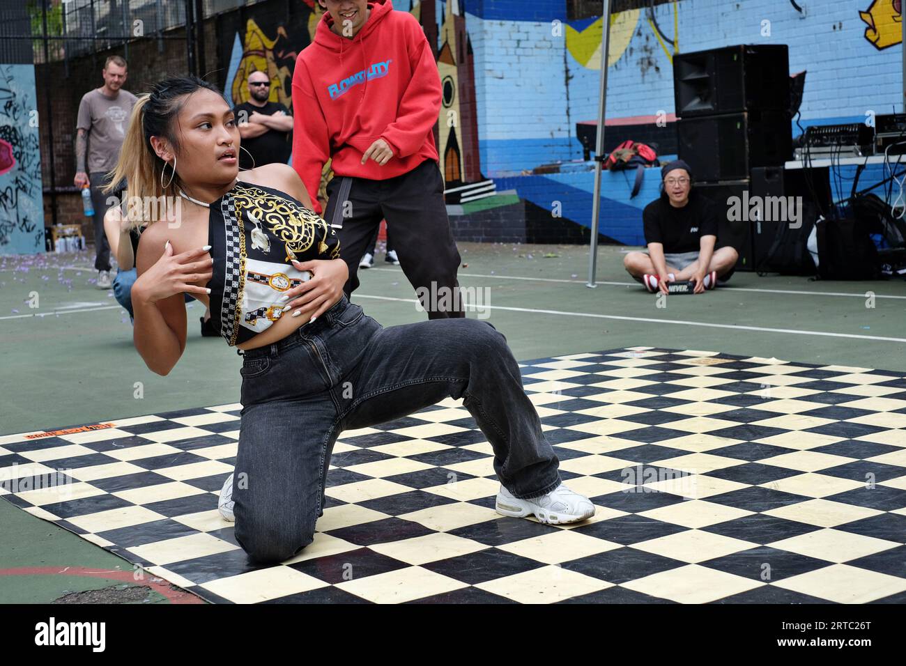 Kneeling woman dancer during a team hip hop battle with great expression as her dance partner looks on during a Breakdancing competition in Sydney Stock Photo