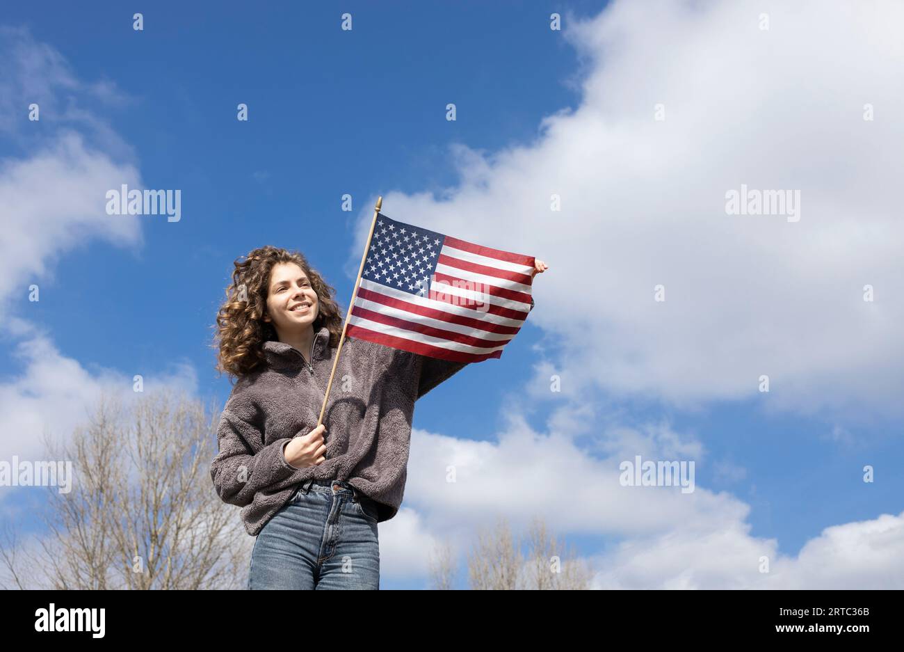 beautiful girl of 18 years old holds an American flag in hands against blue sky on sunny day. holiday . Independence Day of the United States of Ameri Stock Photo