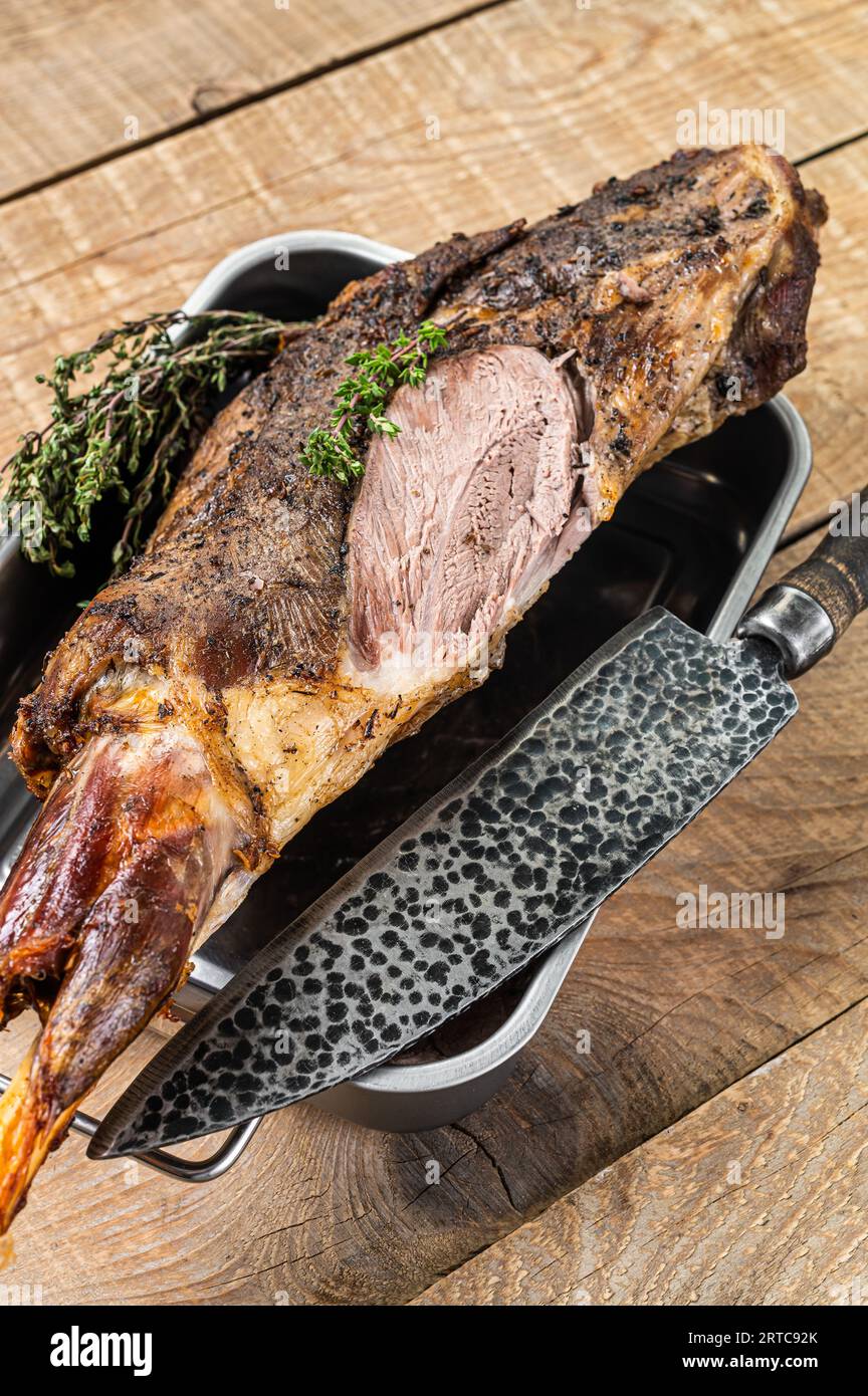 Whole oven roasted goat leg meat with thyme in a steel tray. Wooden