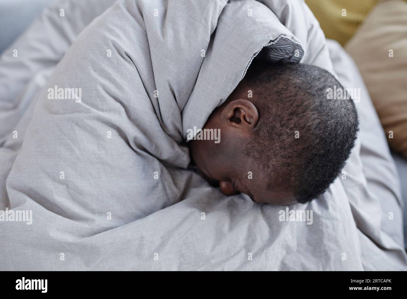 Minimal portrait of depressed black man wrapped in blanket struggling