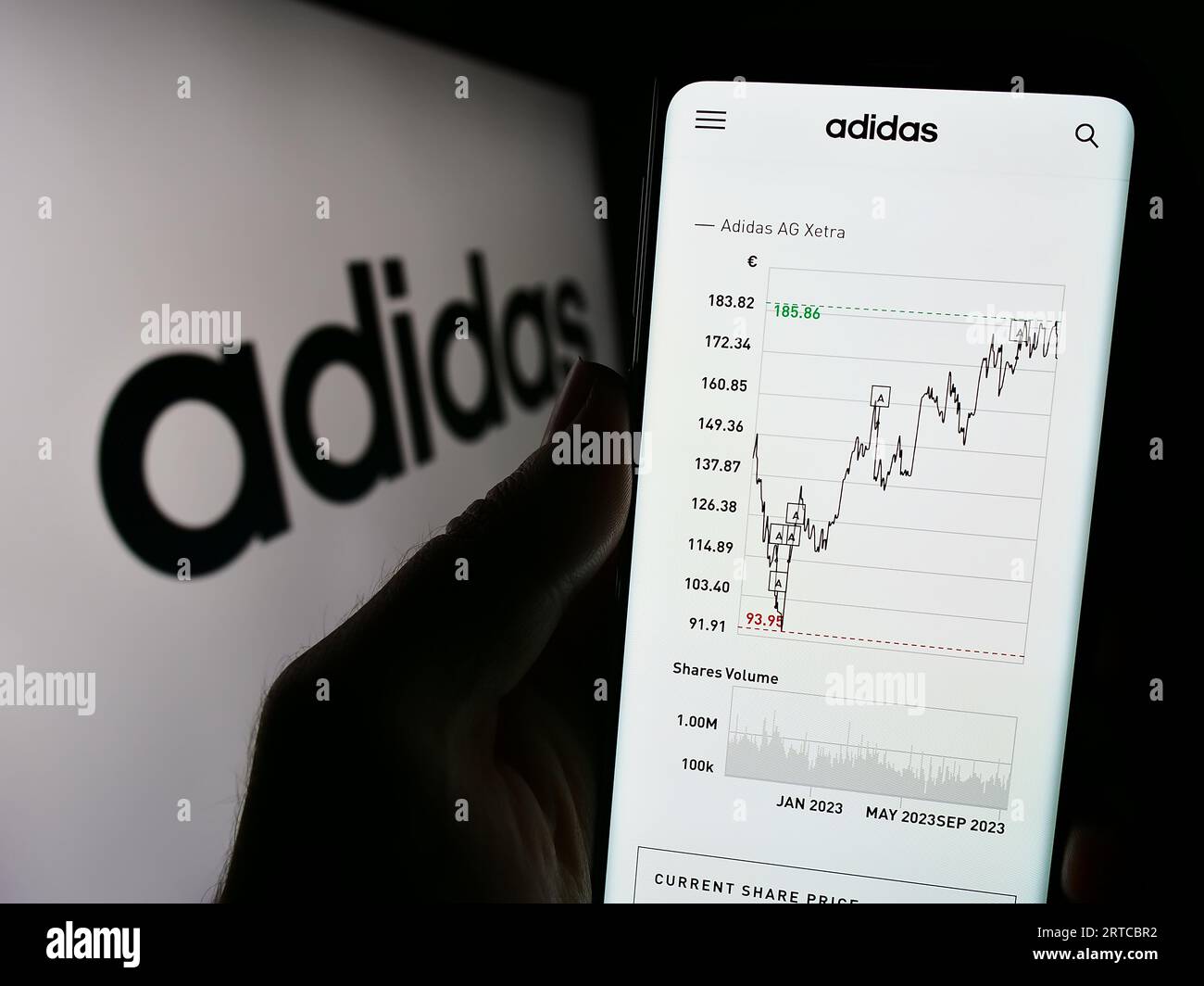 Person holding cellphone with webpage of German apparel and footwear company Adidas AG on screen with logo. Focus on center of phone display. Stock Photo