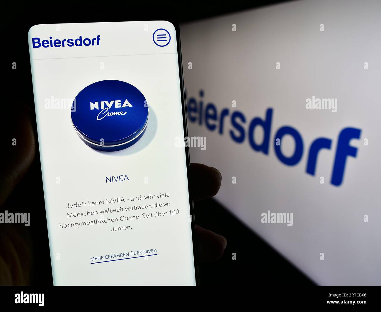 Person holding cellphone with web page of German consumer goods company Beiersdorf AG on screen with logo. Focus on center of phone display. Stock Photo