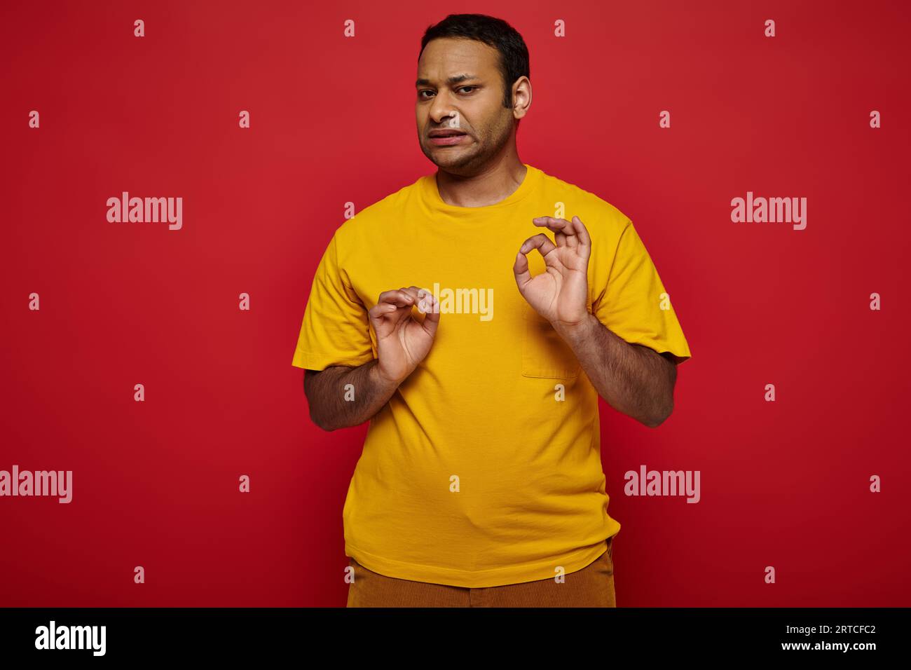emotional indian man in bright casual clothes making disgusted expression on red background Stock Photo