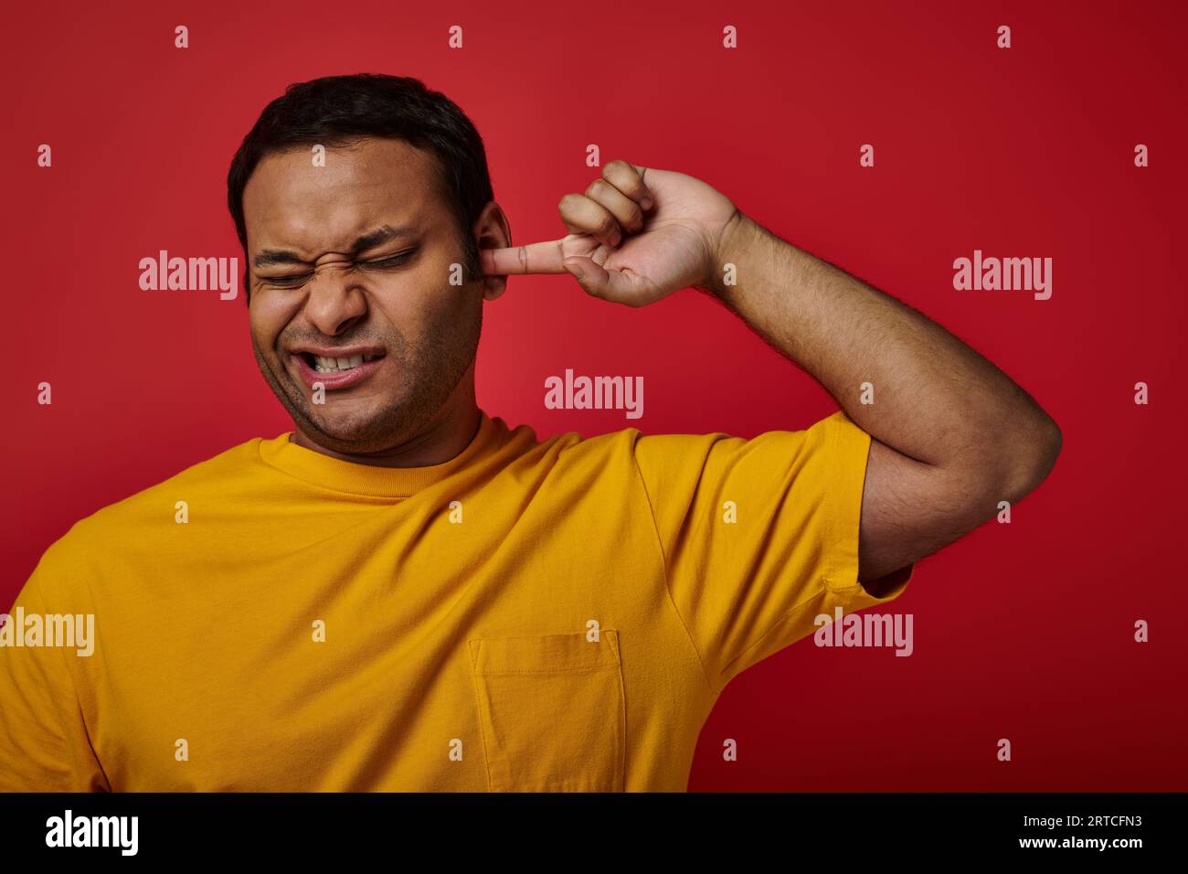 indian man in yellow tshirt closing eyes and picking his ear with