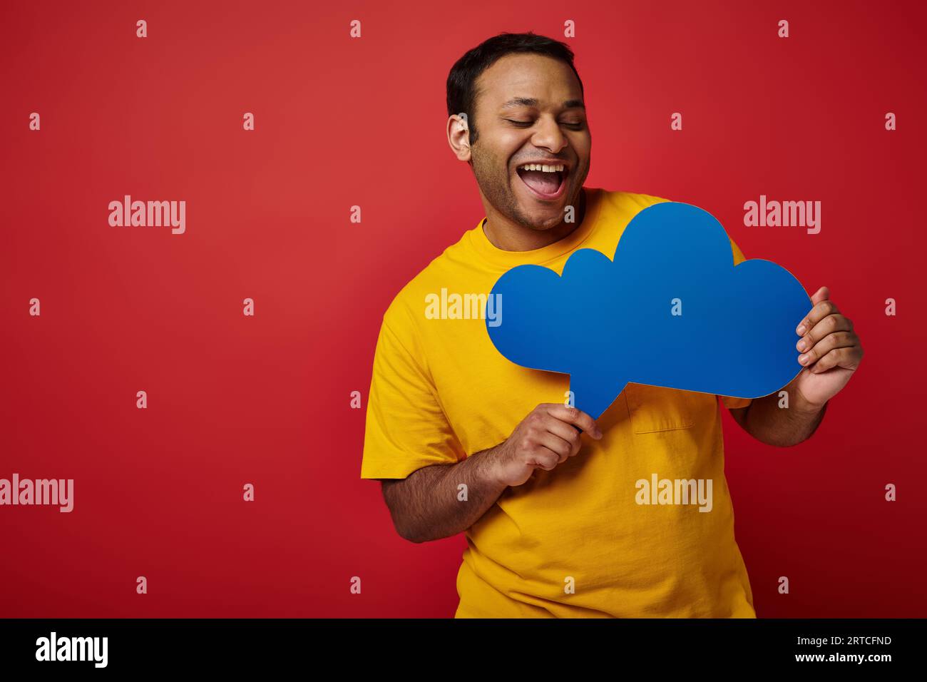 excited man in yellow t-shirt looking at blank thought bubble on red backdrop, cheerful face Stock Photo