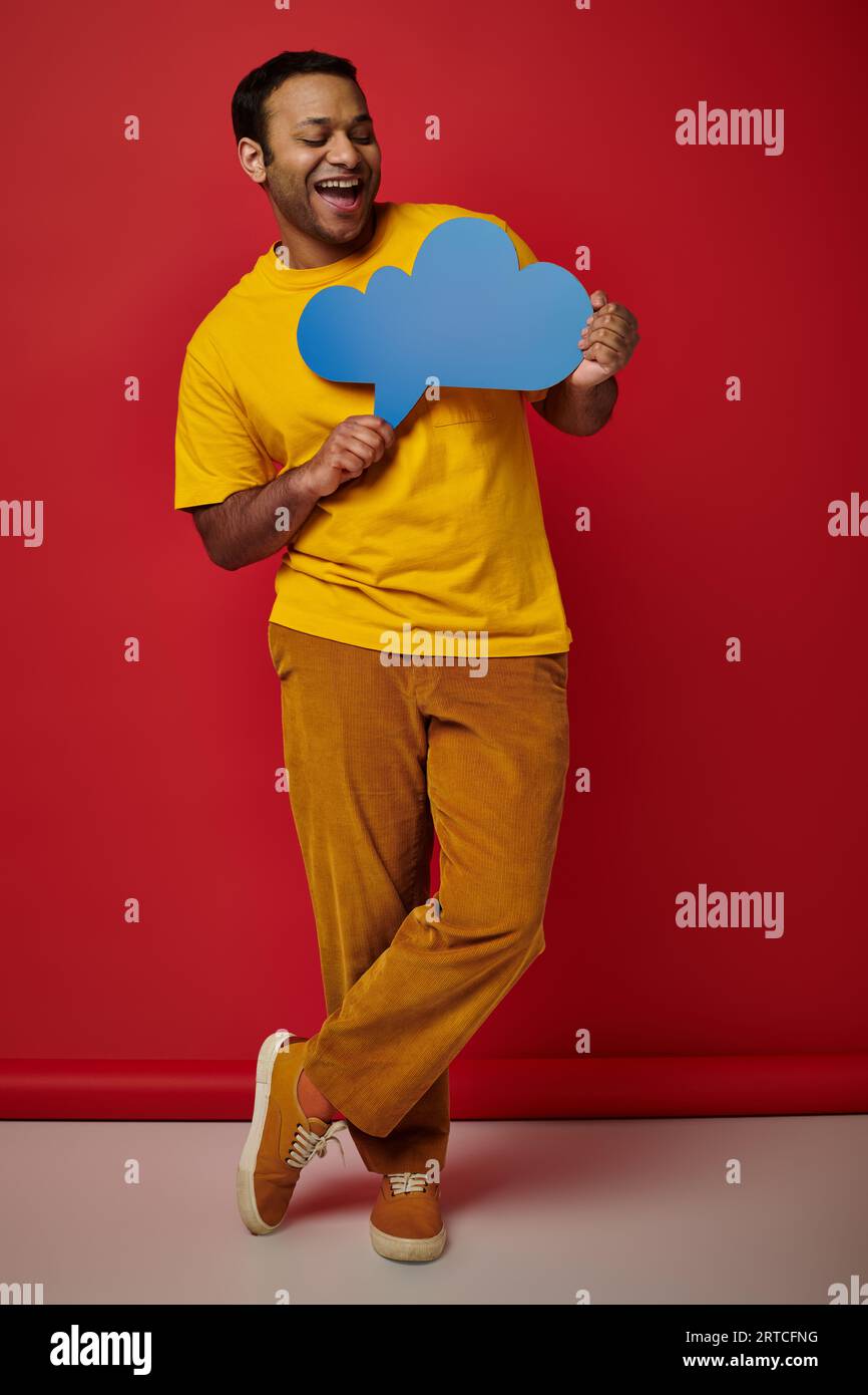 happy man in yellow t-shirt holding blank thought bubble on red backdrop, cheerful face Stock Photo