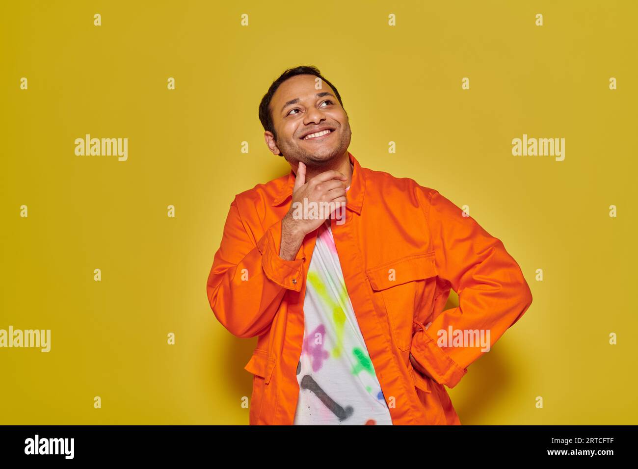 cheerful indian man in orange jacket and diy t-shirt standing with hand ...