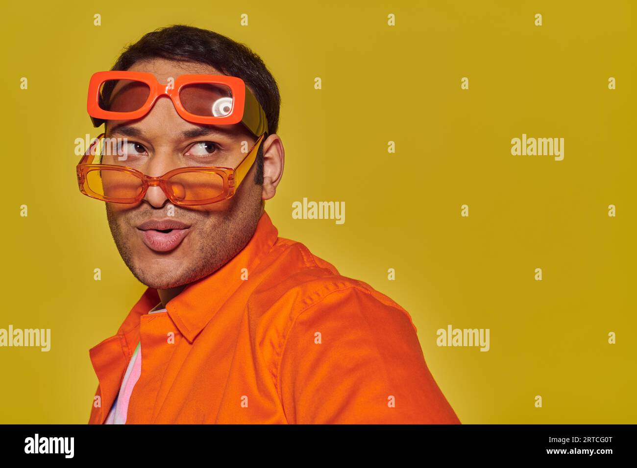 fashionable indian man trying on different trendy sunglasses and looking away on yellow backdrop Stock Photo