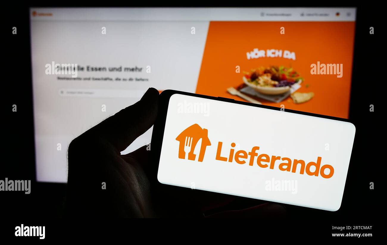 Person holding smartphone with logo of German food delivery company Lieferando on screen in front of website. Focus on phone display. Stock Photo