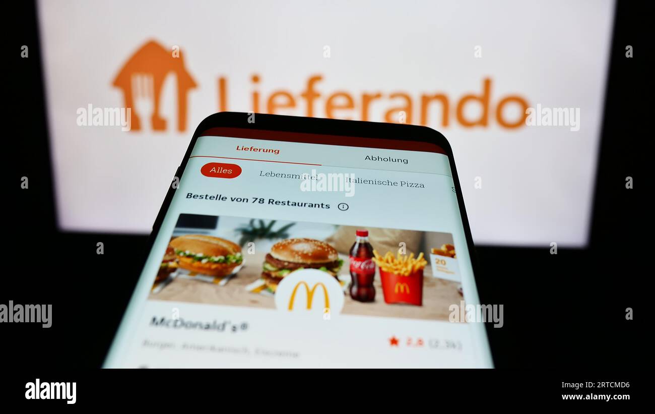 Mobile phone with website of German food delivery company Lieferando on screen in front of business logo. Focus on top-left of phone display. Stock Photo