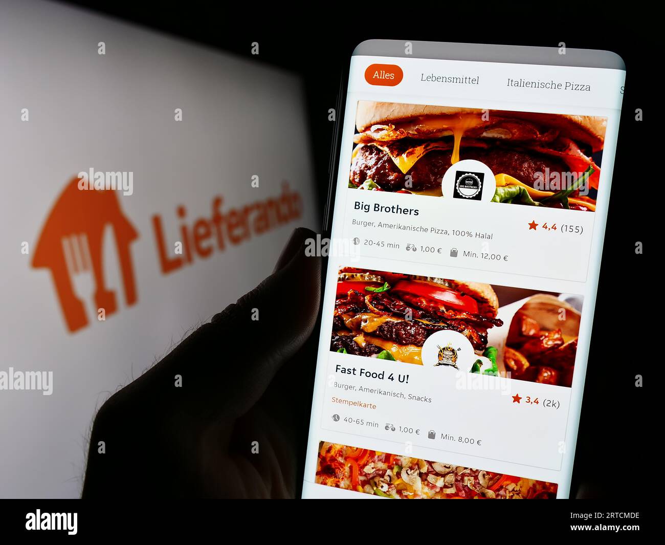 Person holding smartphone with webpage of German food delivery company Lieferando on screen in front of logo. Focus on center of phone display. Stock Photo