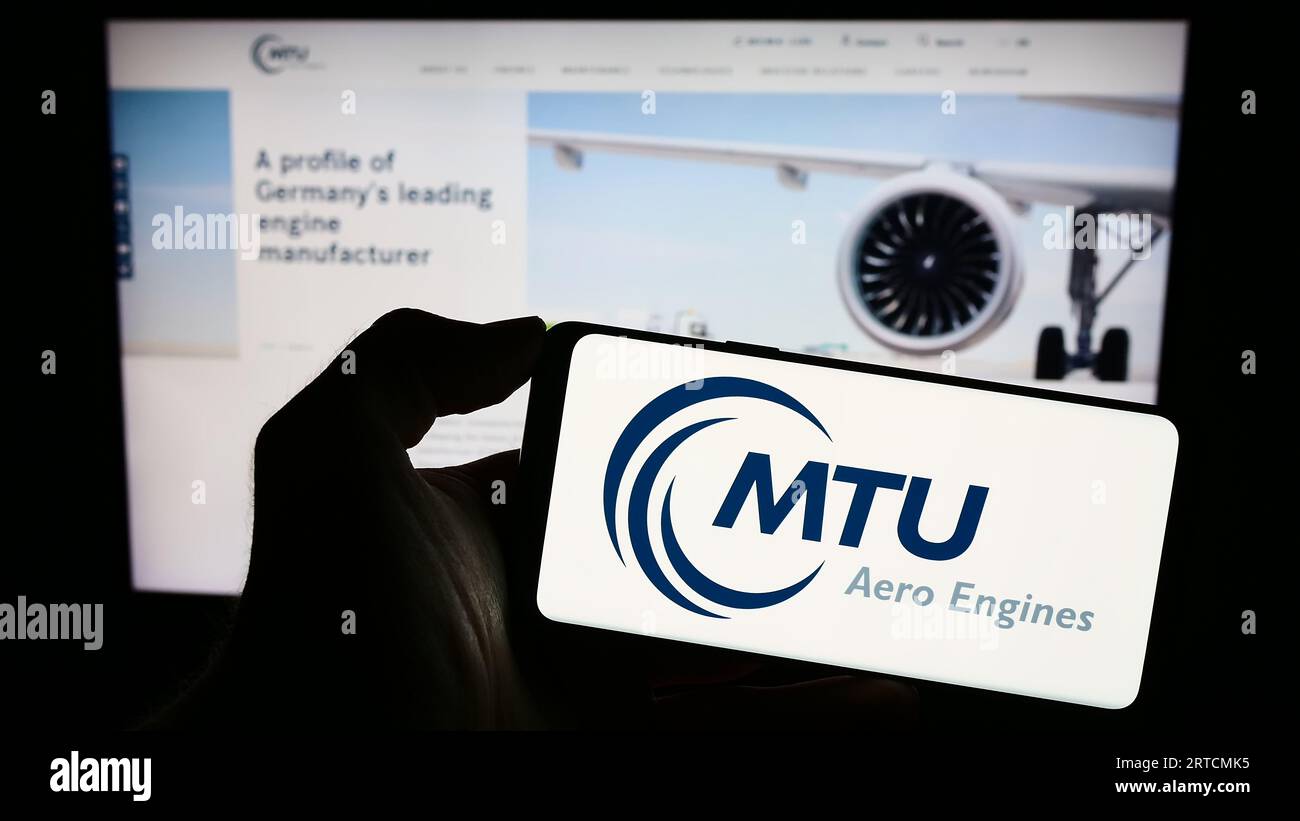 Person holding smartphone with logo of German aviation company MTU Aero Engines AG on screen in front of website. Focus on phone display. Stock Photo