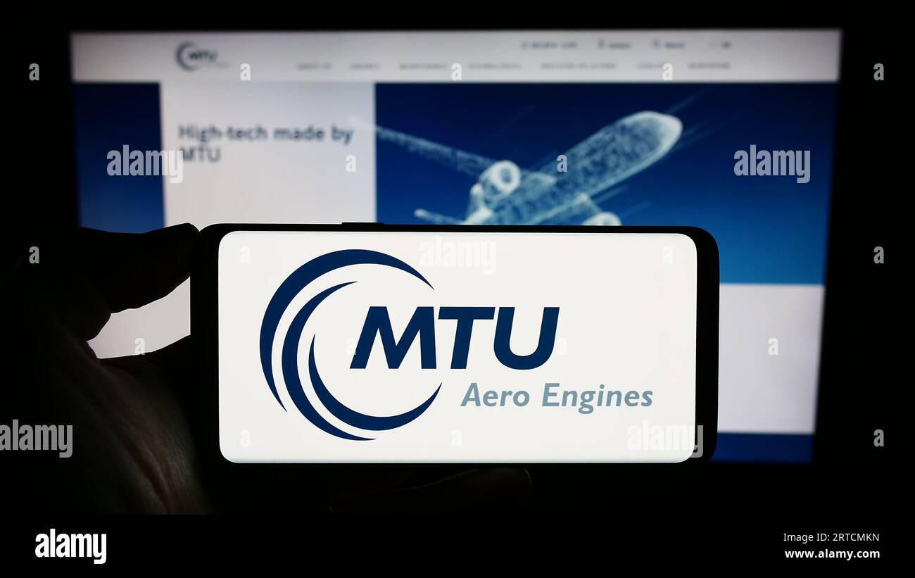 Person holding cellphone with logo of German aviation company MTU Aero Engines AG on screen in front of business webpage. Focus on phone display. Stock Photo