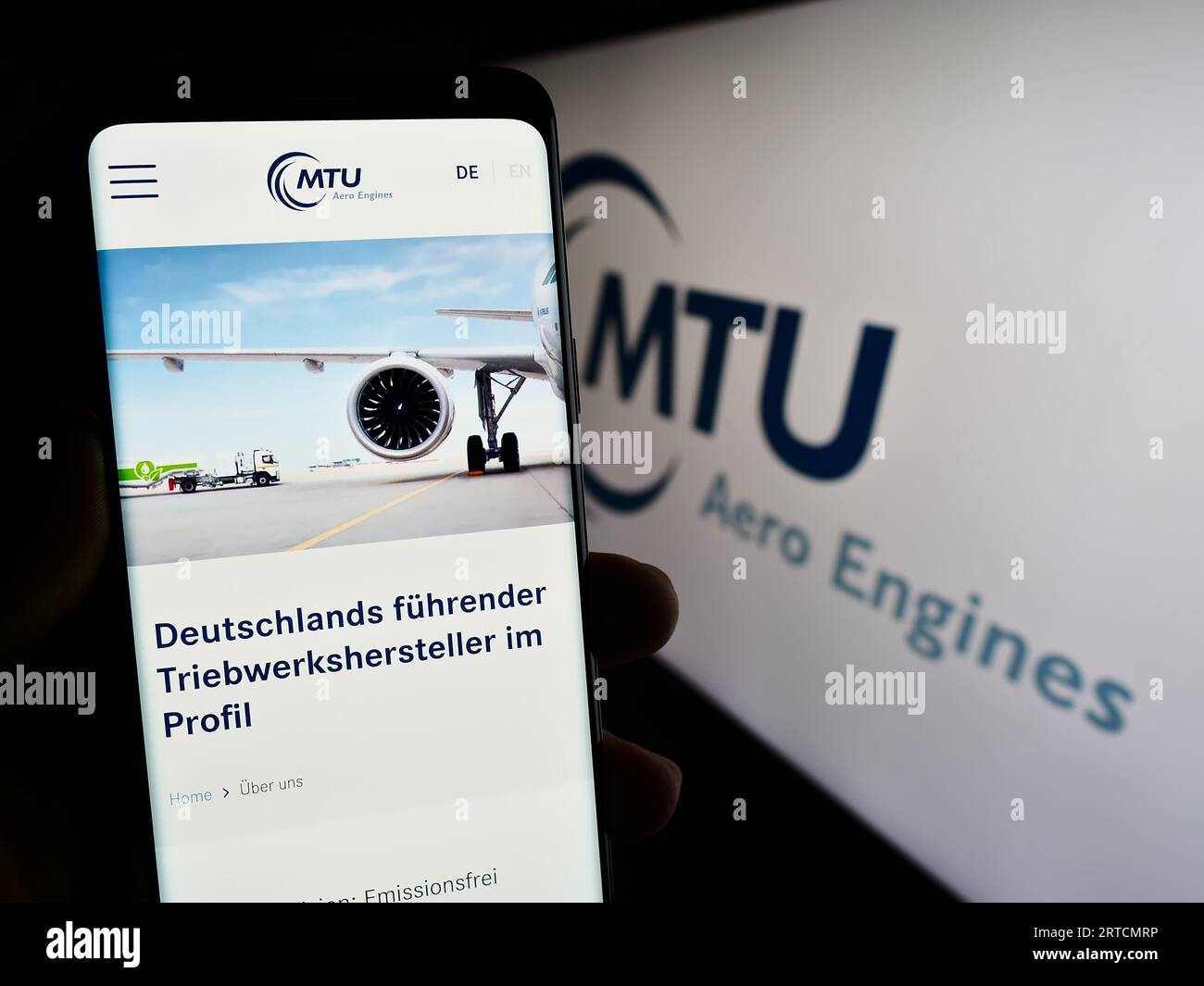 Person holding mobile phone with web page of German aviation company MTU Aero Engines AG on screen with logo. Focus on center of phone display. Stock Photo
