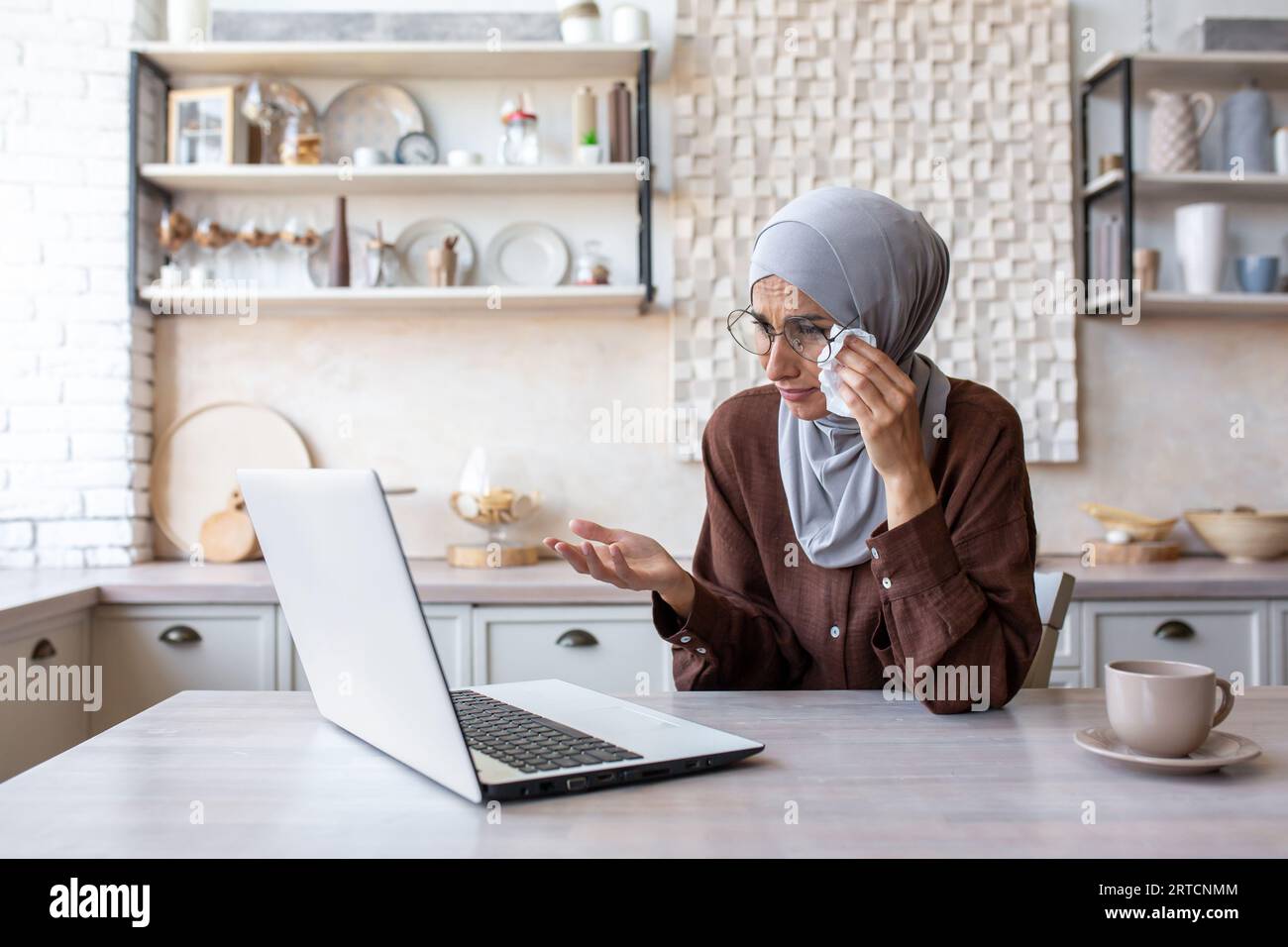 Muslim woman in hijab sitting in kitchen at home and crying in front of ...