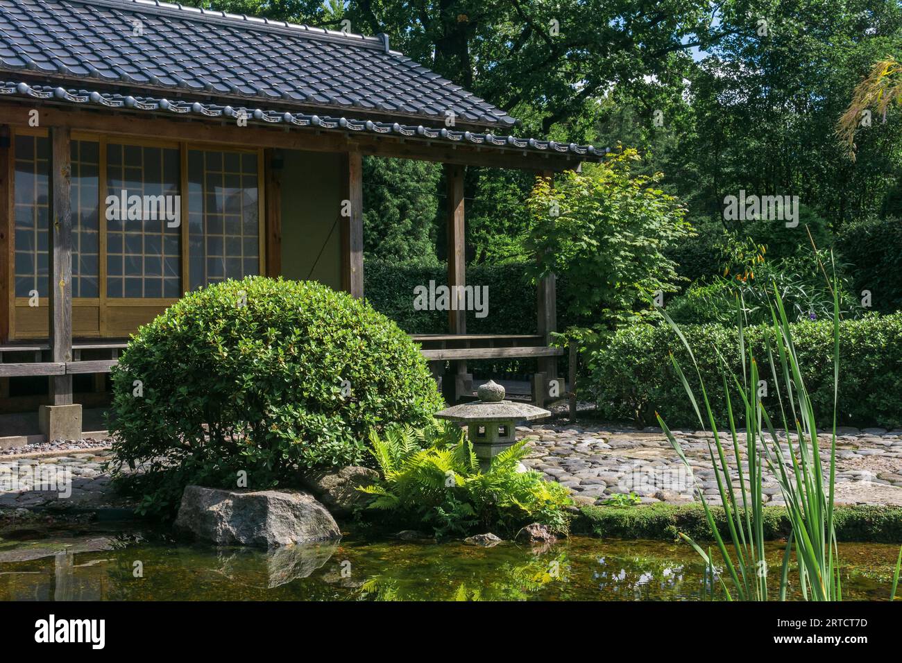tea house and stone lantern behind pond in japanese garden Stock Photo
