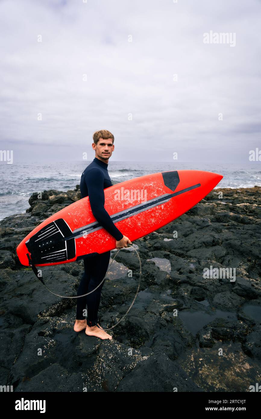 happy surfer, with blonde hair, looking at the waves before going into the surf on a cloudy day Stock Photo