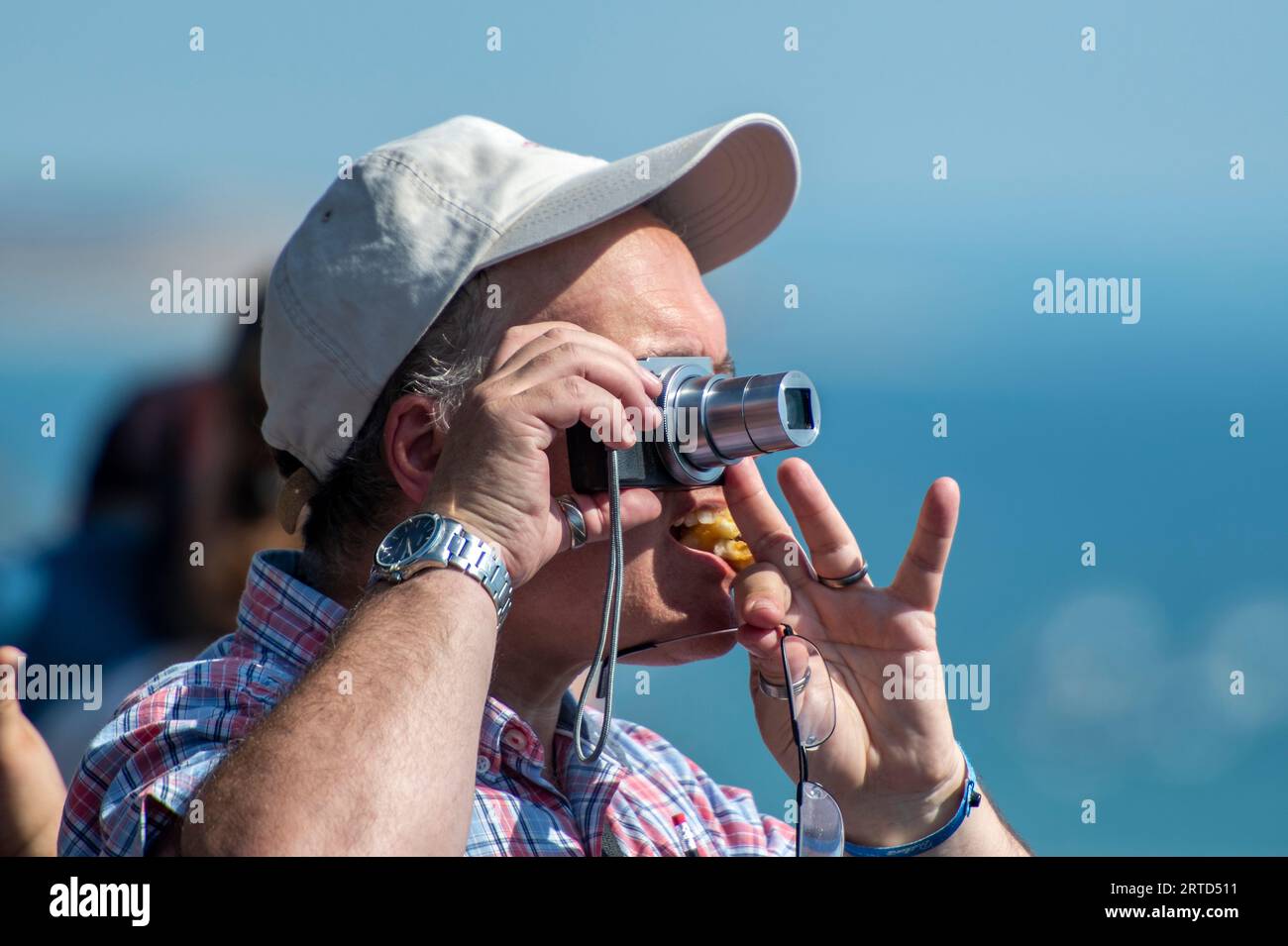 middle aged man wearing a baseball cap using a small digital camera to take a photograph. Stock Photo