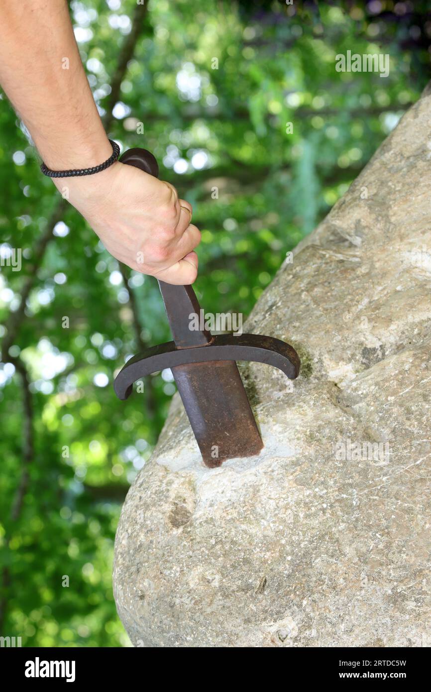 hand forcefully extracts the sword stuck in the rock as in the mythological story of King Arthur Stock Photo
