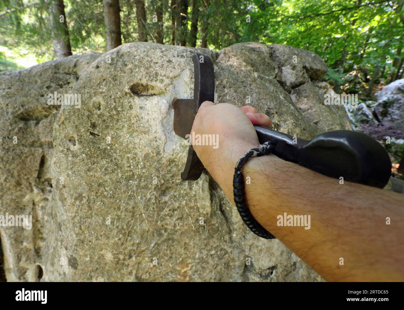 hand forcefully extracts the sword stuck in the rock as in the mythological tale of King Arthur Stock Photo