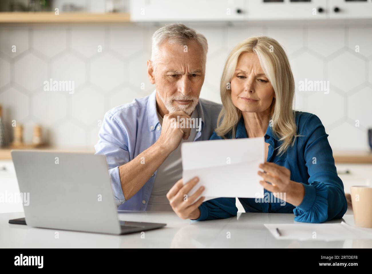 Senior Couple Checking Financial Documents While Sitting In Kitchen At Home Stock Photo