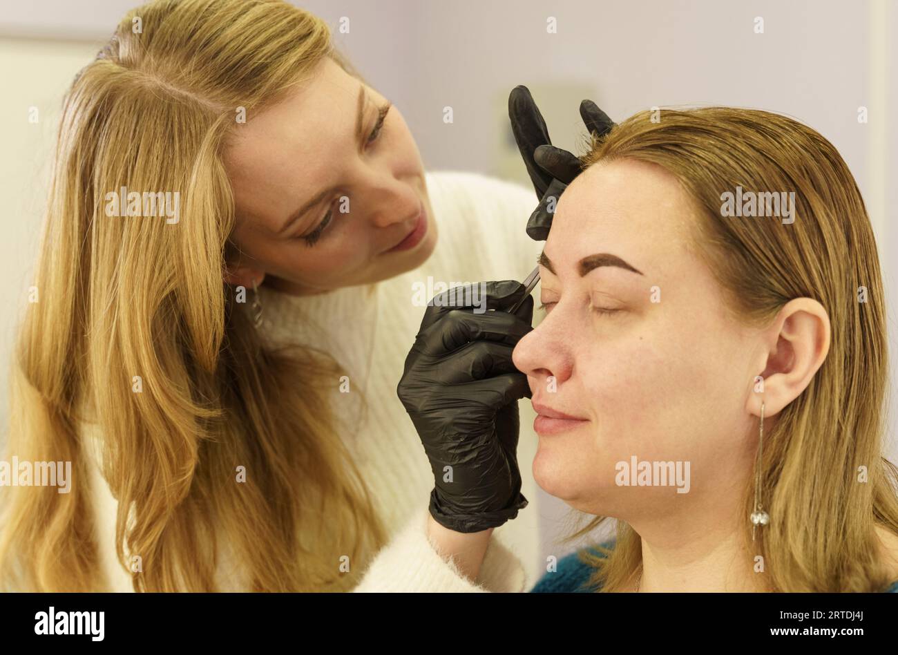 Portrait of a woman having her eyebrows plucked with tweezers in a beauty salon. Beauty industry. Stock Photo