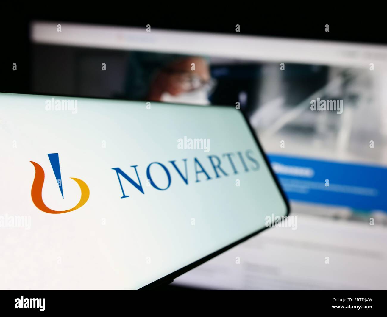 Mobile phone with logo of Swiss pharmaceutical company Novartis AG on screen in front of business website. Focus on left of phone display. Stock Photo