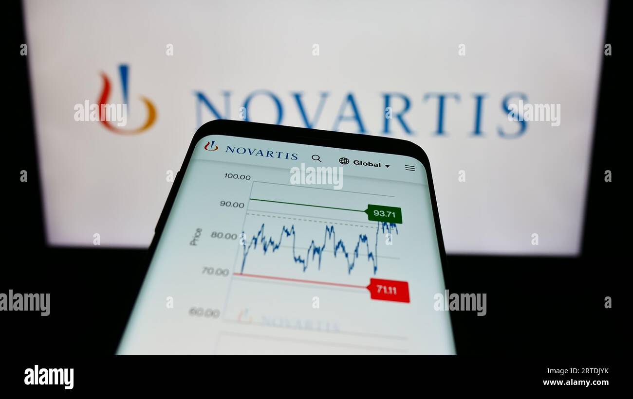 Smartphone with website of Swiss pharmaceutical company Novartis AG on screen in front of business logo. Focus on top-left of phone display. Stock Photo