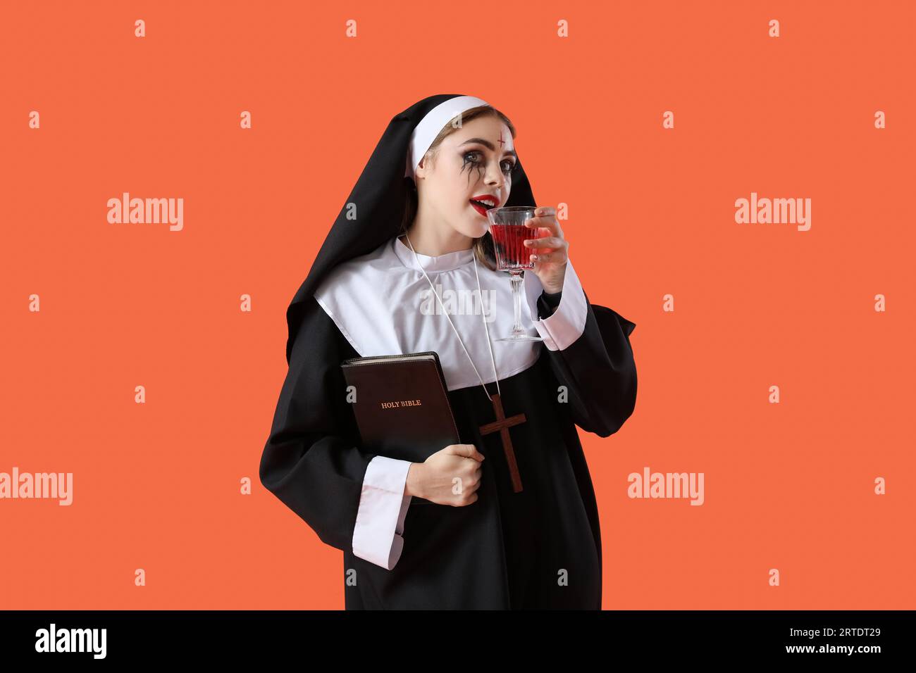 Young woman dressed for Halloween as nun drinking on red background Stock Photo