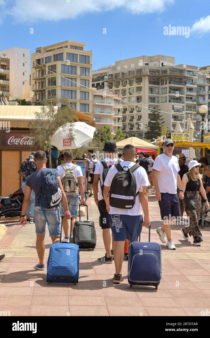Sliema, Malta - 6 August 2023: Young people pulling suitcases along the promenade in Sliema. Stock Photo