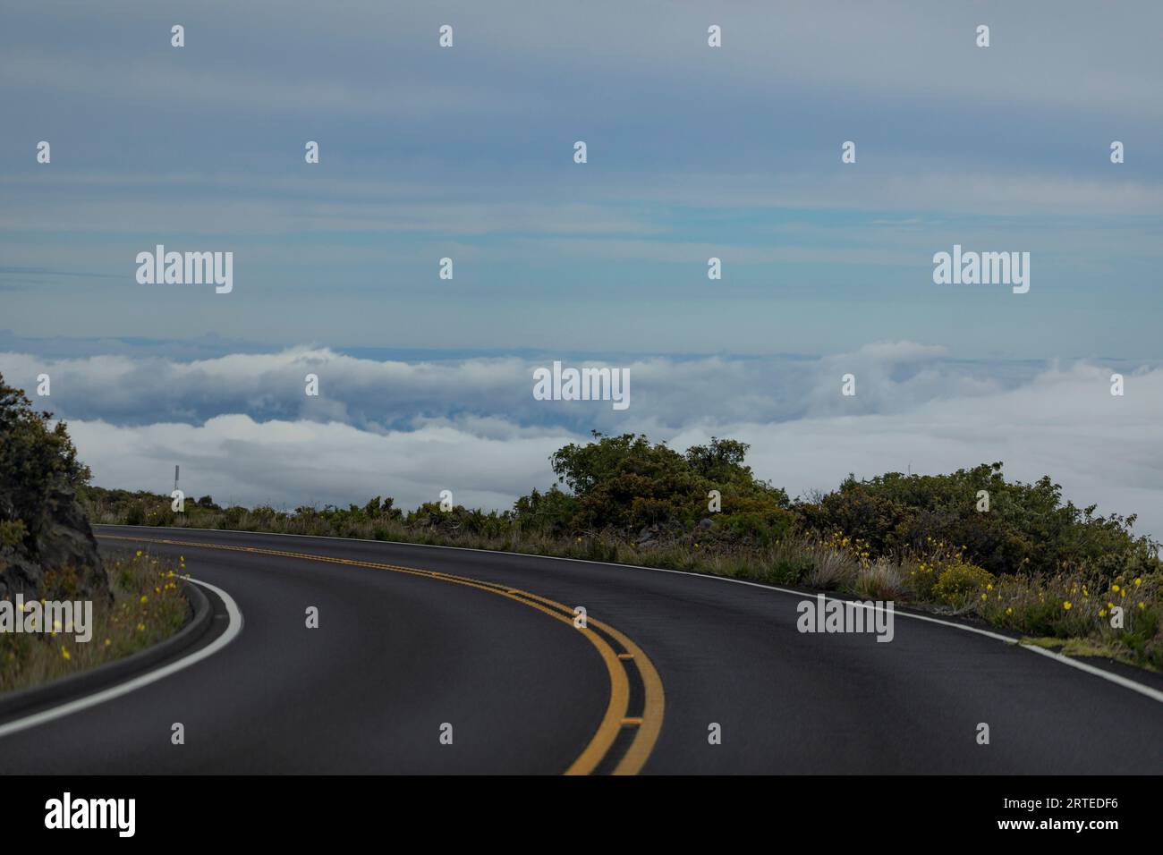 Close-up of a sharp turn in the paved highway with view from above the clouds on the mountainside on the Road down from Haleakala Stock Photo