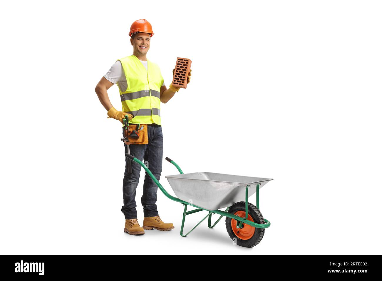 Construction worker holding a brick and standing behind a wheelbaroow isolated on white background Stock Photo