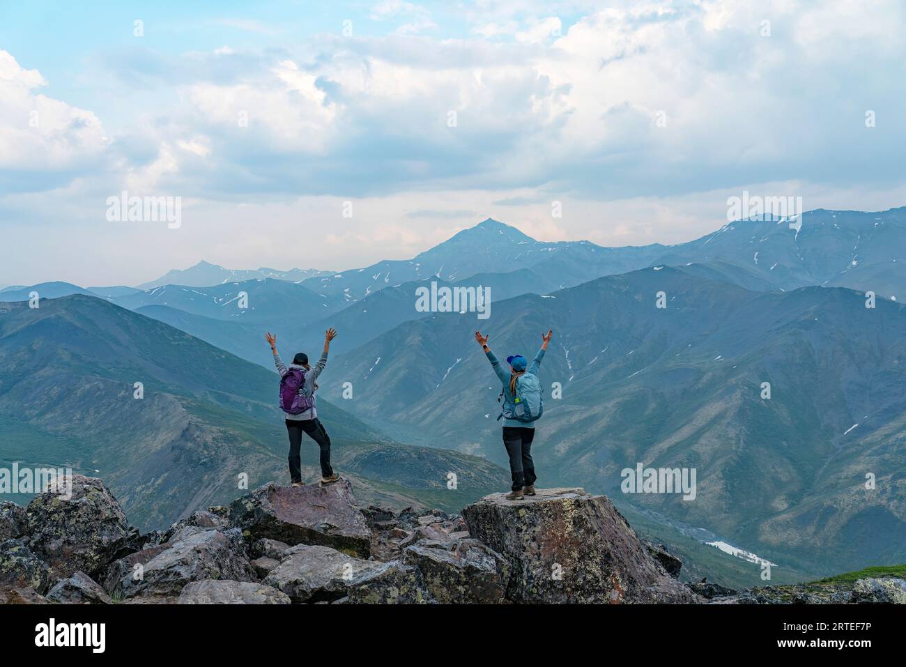 Two women standing on a rocky mountain top with their arms raised in the air in celebration, enjoying the view of the amazing scenery in Northern Y... Stock Photo