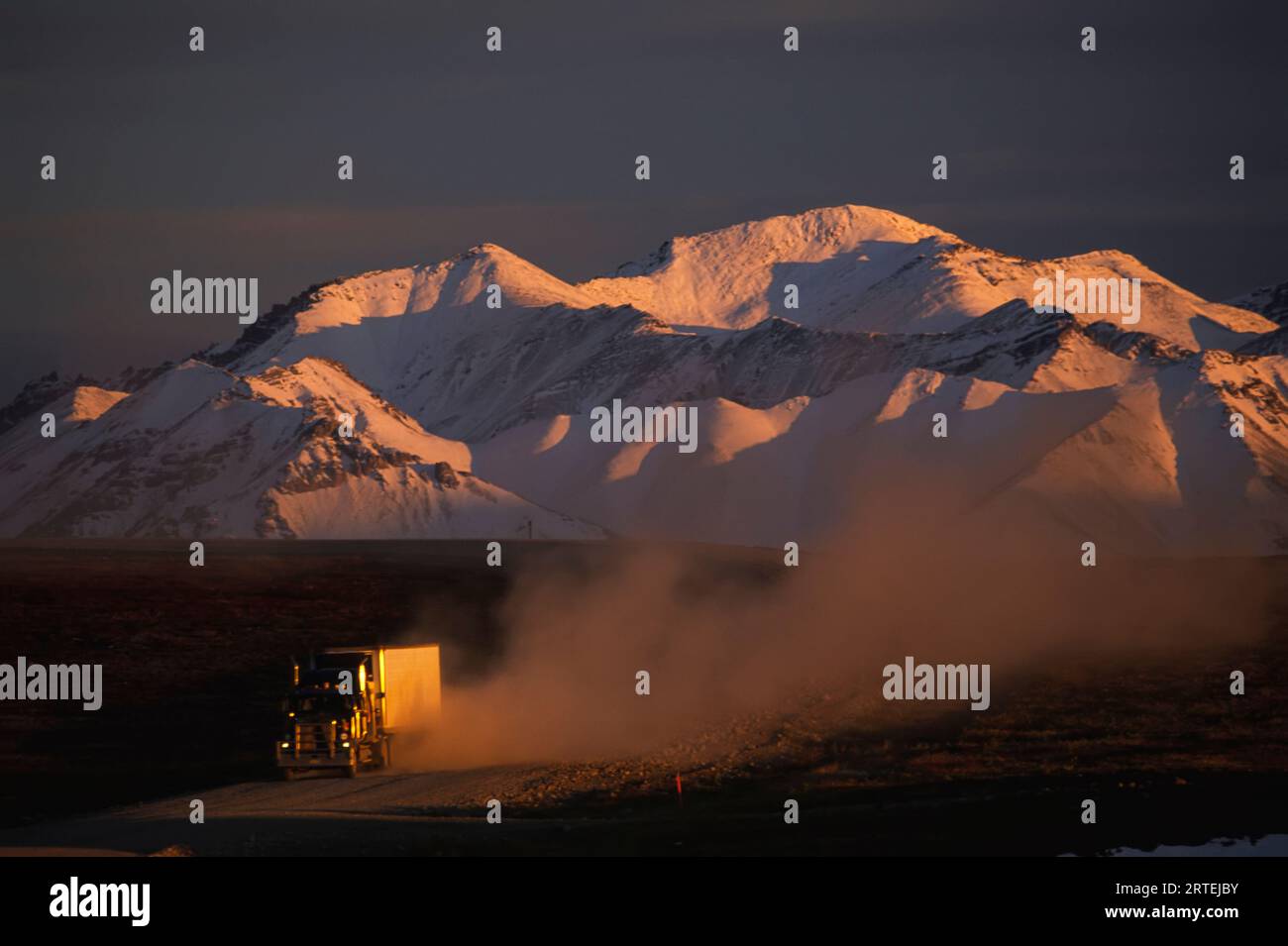 Transport truck speeds along the Dalton Highway with snow-covered mountains in the background; Alaska, United States of America Stock Photo