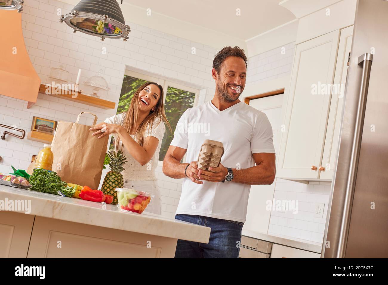 Smiling couple with paper shopping bag and groceries in kitchen Stock Photo