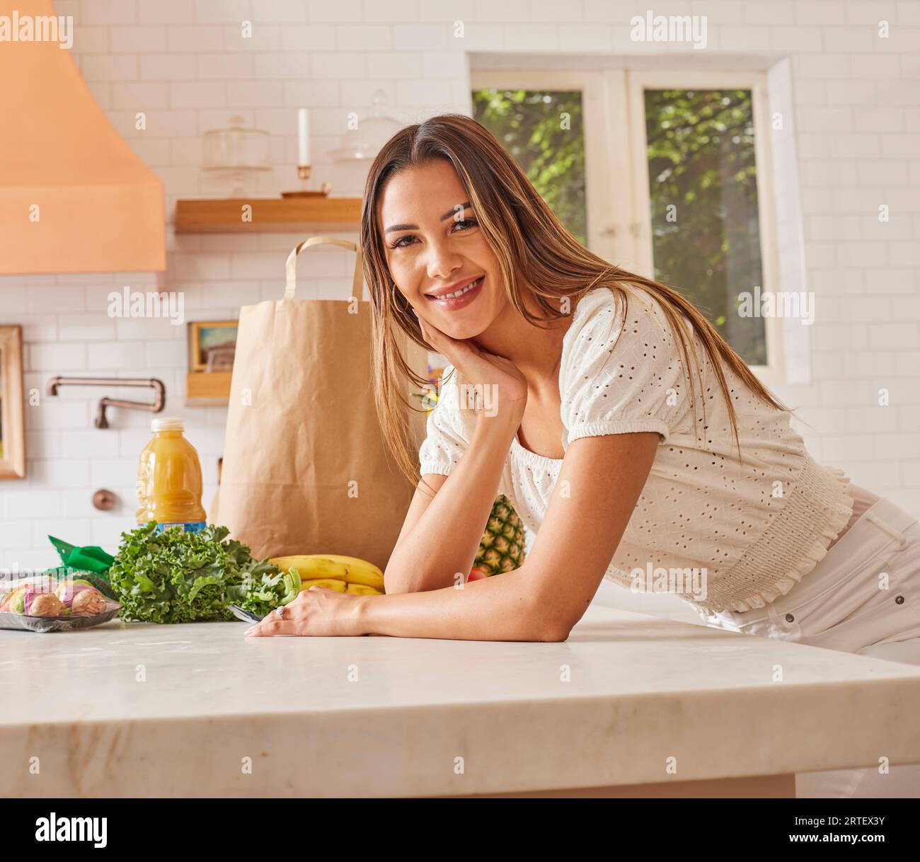 Portrait of smiling woman with paper shopping bag and groceries in kitchen Stock Photo