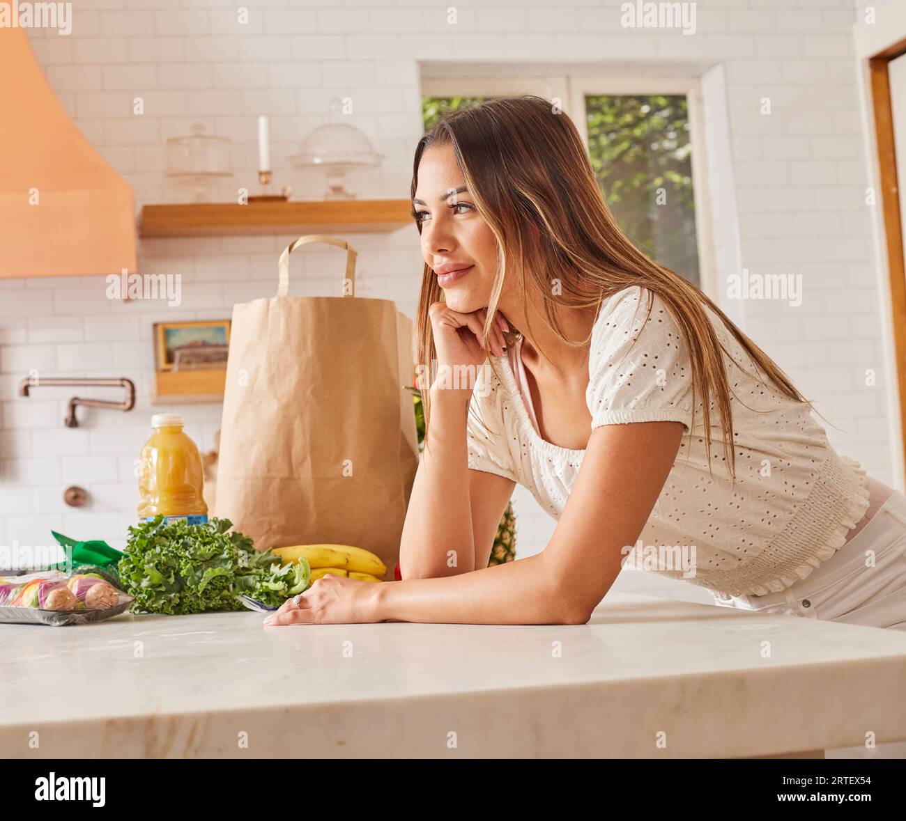 Smiling woman with paper shopping bag and groceries in kitchen Stock Photo