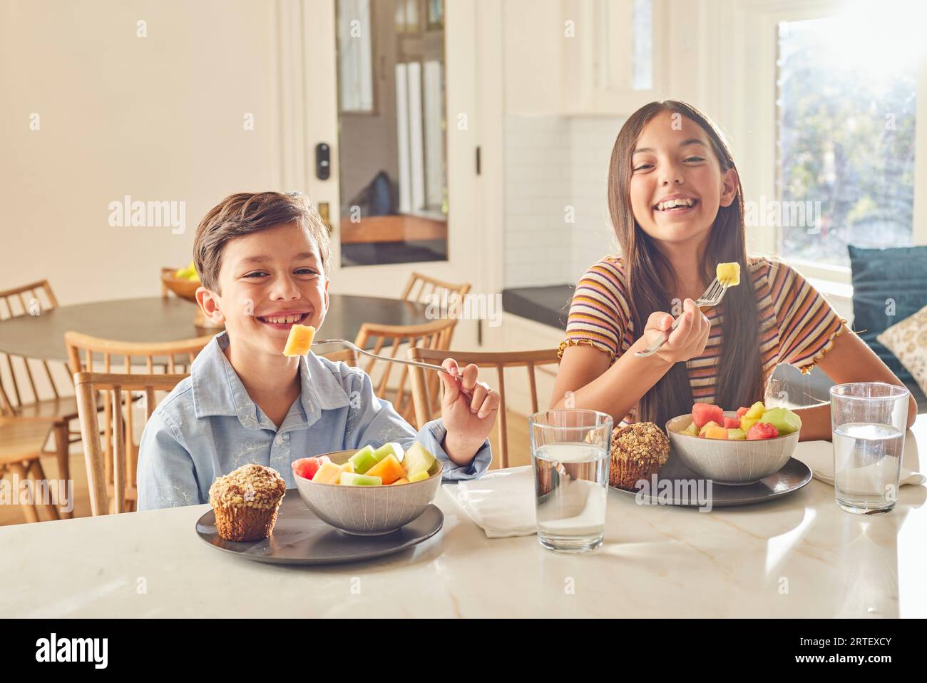 Smiling boy (8-9) and girl (12-13) enjoying breakfast in kitchen Stock Photo