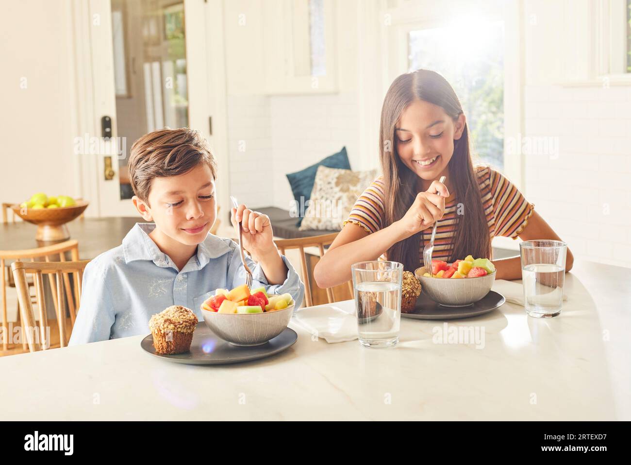 Smiling boy (8-9) and girl (12-13) having breakfast in kitchen Stock Photo
