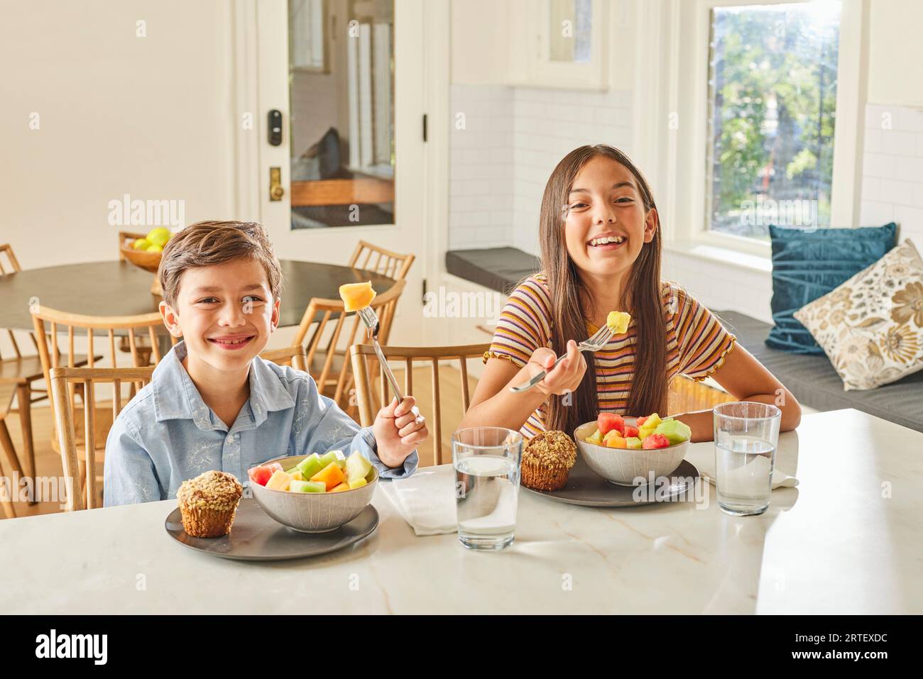 Smiling boy (8-9) and girl (12-13) enjoying breakfast in kitchen Stock Photo