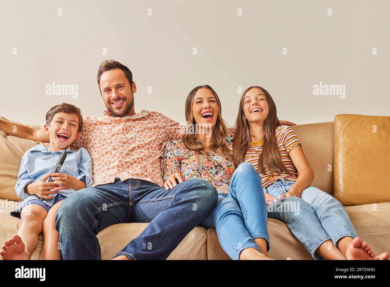 Smiling family with two children (8-9, 12-13) watching TV on sofa Stock Photo