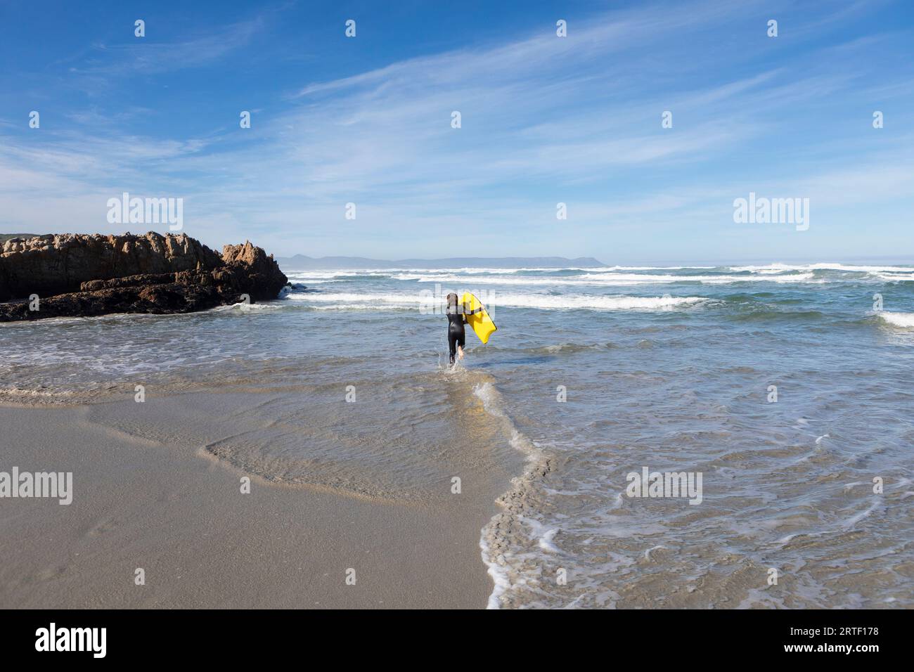 South Africa, Hermanus, Boy (10-11) entering Atlantic Ocean with body board in Kammabaai Beach Stock Photo