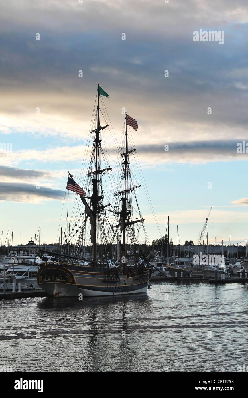 The tall ship Lady Washington lies at anchor in a Pacific Northwest harbor with its masts and rigging in silhouette against the sunset evening sky Stock Photo