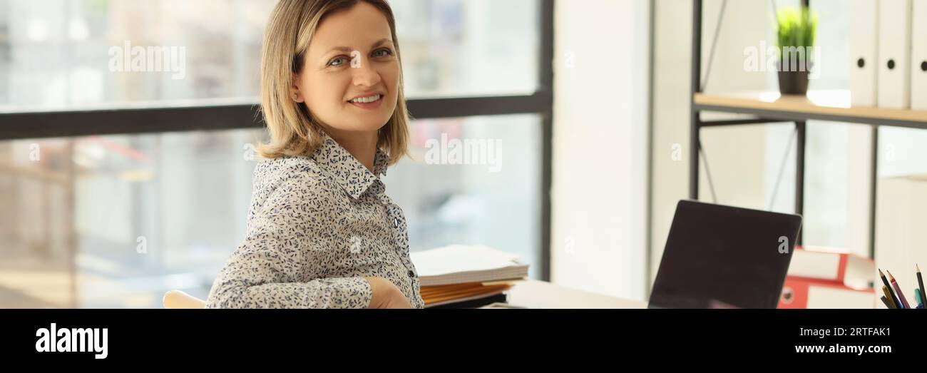 Manager sits at her workplace in office and look at camera. Stock Photo
