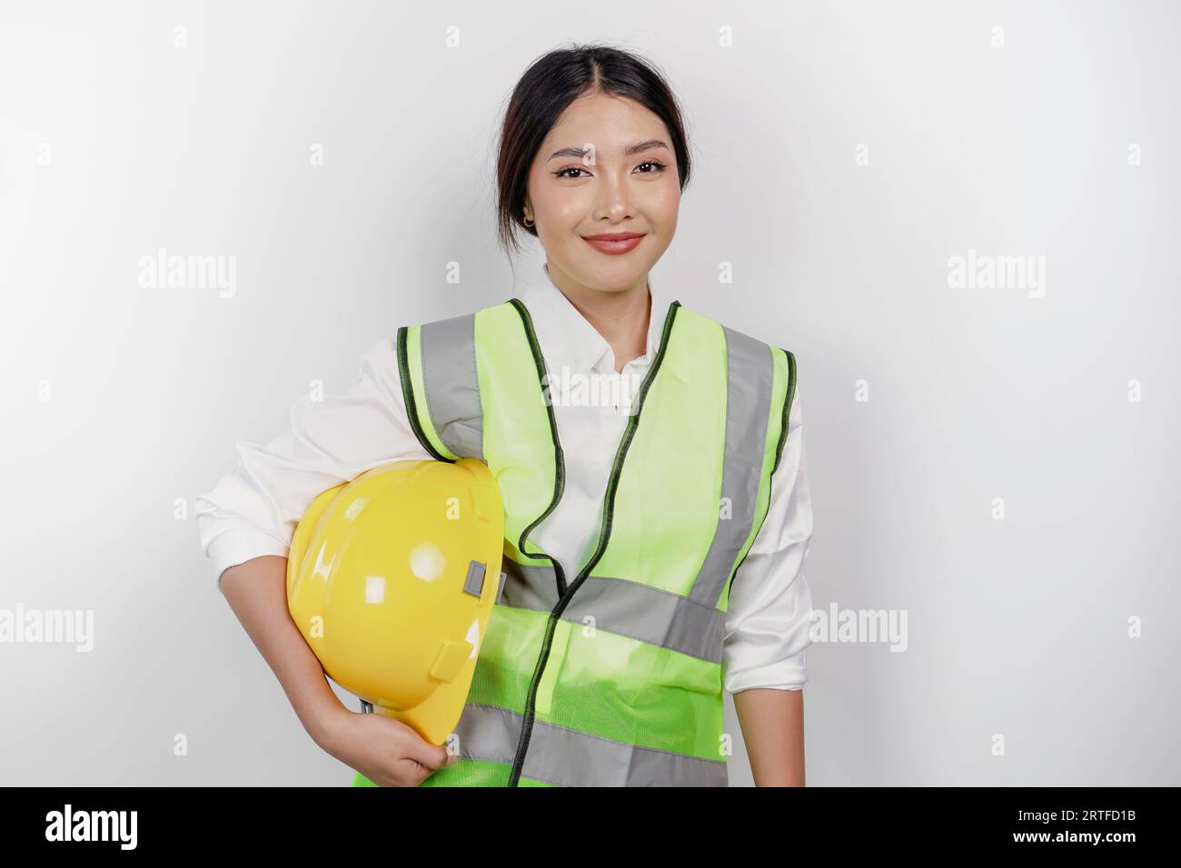 Confident Asian woman labor worker is smiling to the camera, bringing her safety helmet, wearing yellow safety helmet, green vest and uniform, isolate Stock Photo